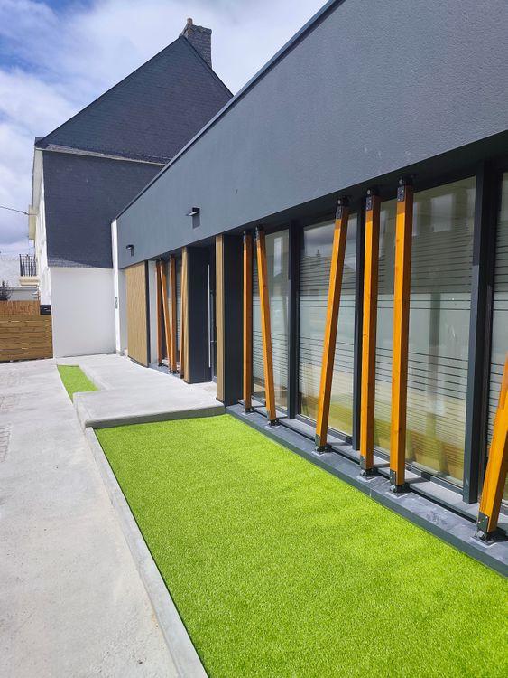 facade avec poteau bois et bardage imitation bois, faux gazon et rampe d'accès PMR, façade enduit anthracite et menuiseries alu ral 7016